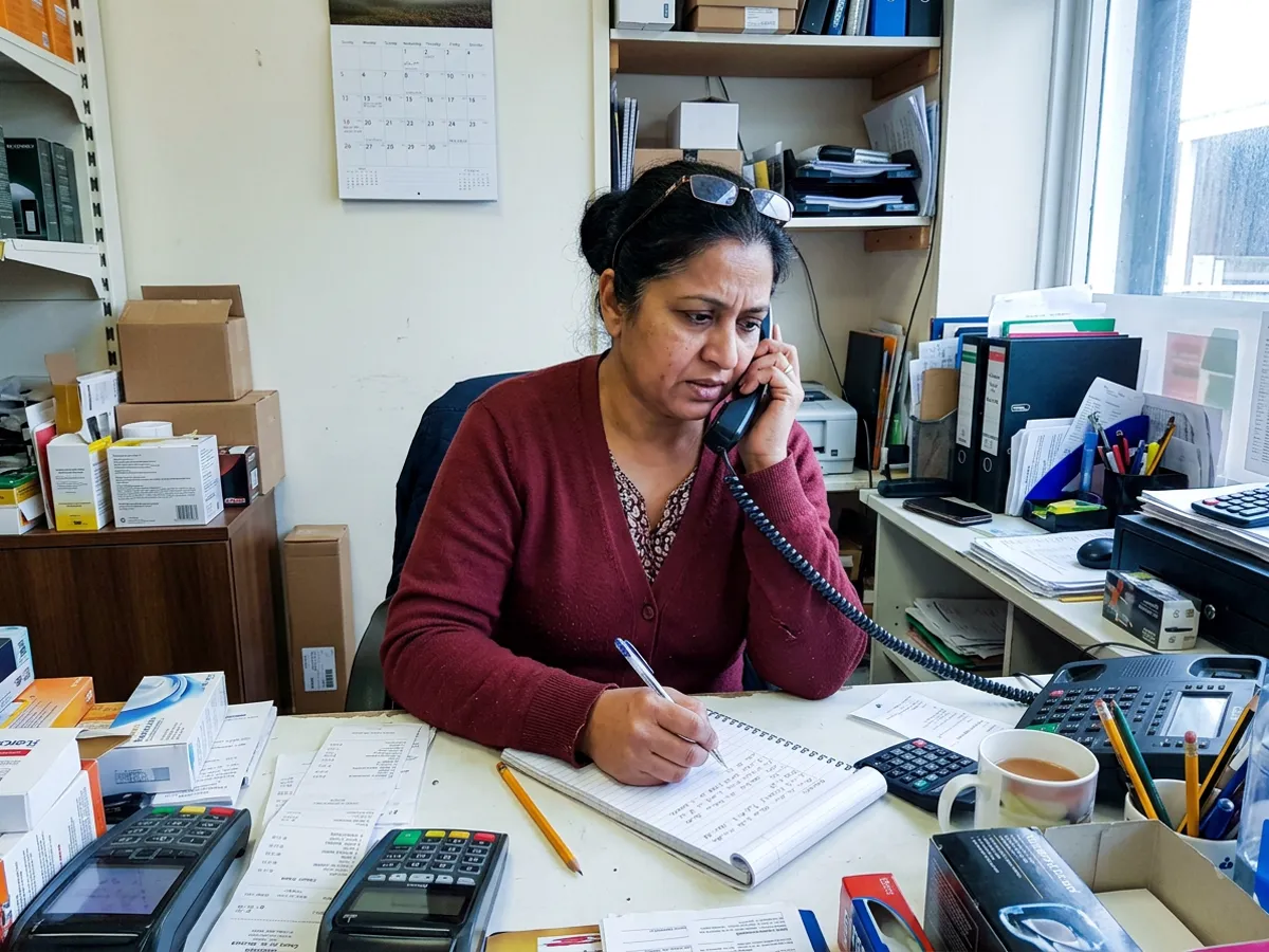 A woman on the phone at a cluttered office desk, taking notes